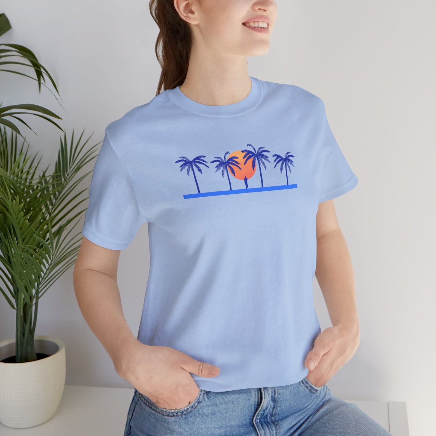 Retro unisex tropical blue t-shirt with blue palm trees and sunset illustration worn by a woman